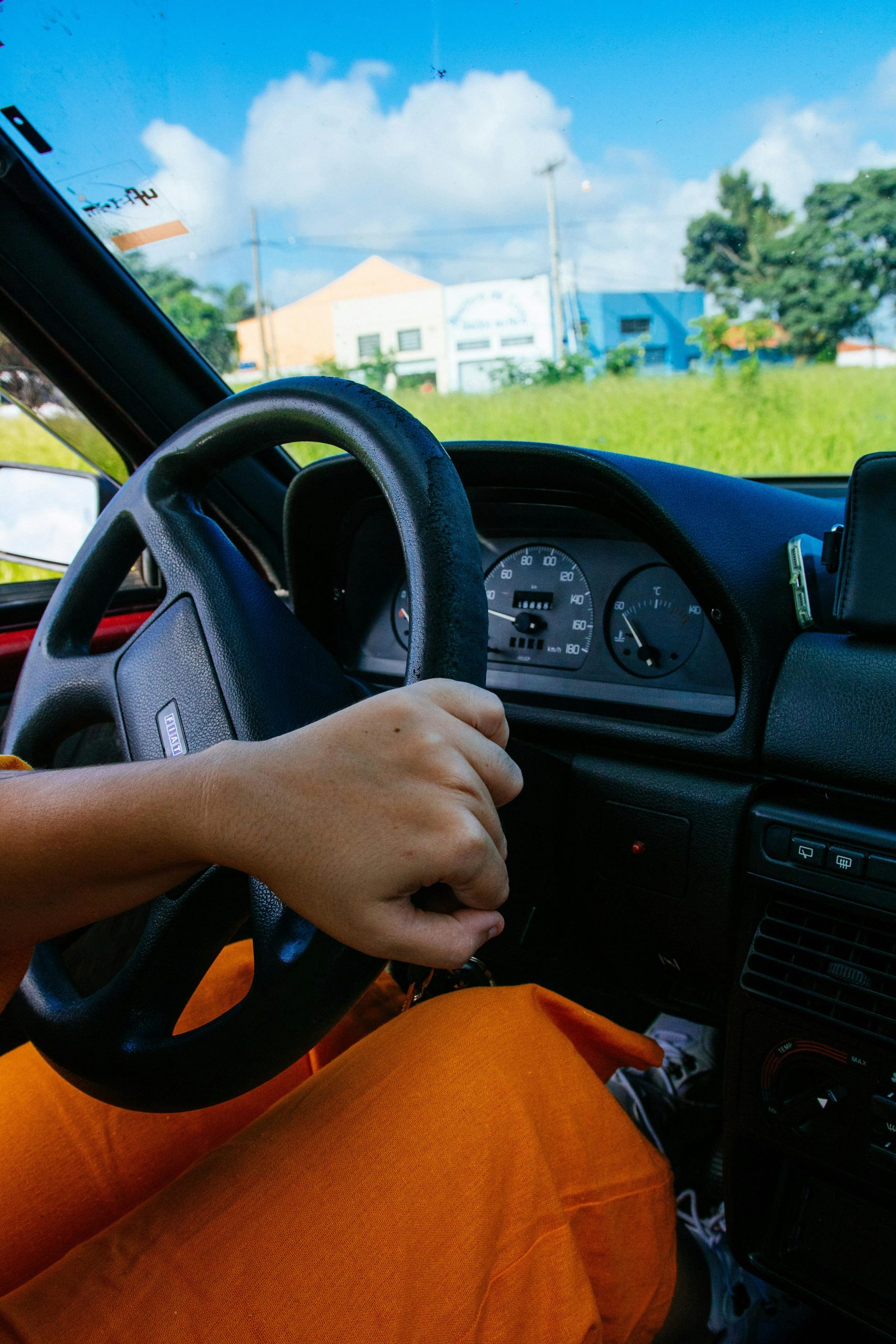 Close-up of a person driving a car, showcasing the steering wheel and dashboard on a sunny day.