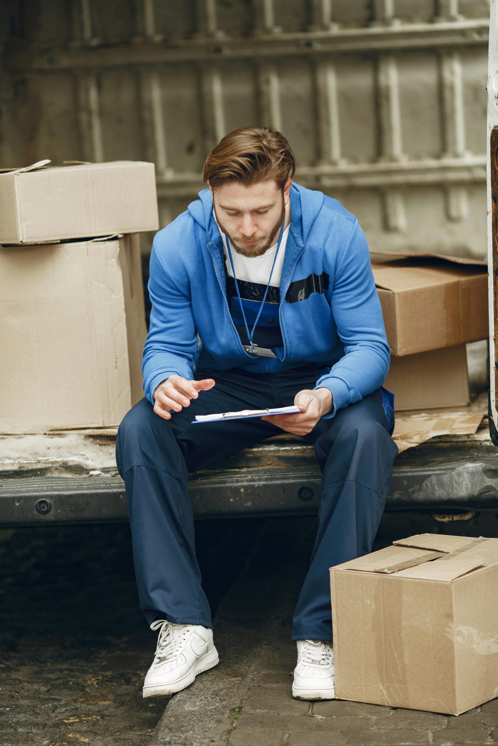 A warehouse employee sitting by a van checking inventory with a tablet device.